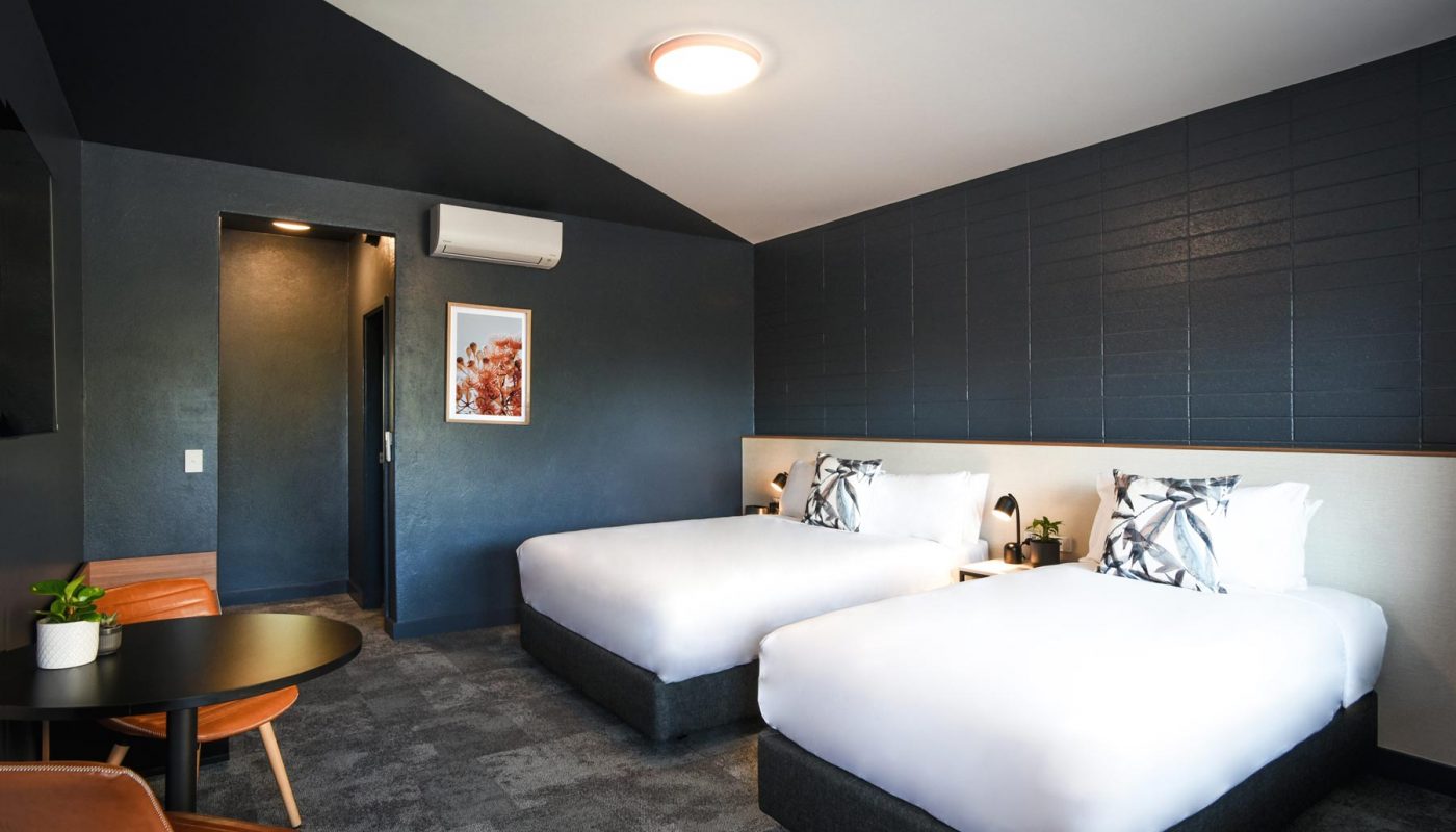 Room with two white beds, dark paneled walls, a small round table and chairs, and a doorway.