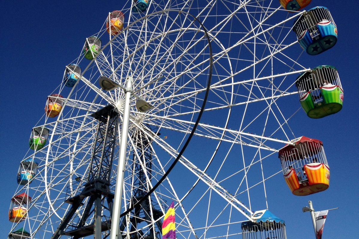 A large white Ferris wheel with colorful gondolas against a clear blue sky, viewed from below.