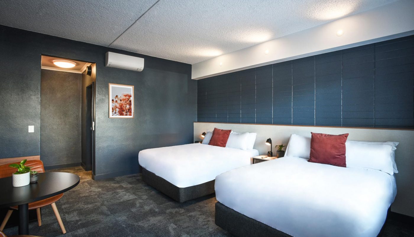 Modern hotel room with two white beds, dark blue paneled walls, and bedside tables.