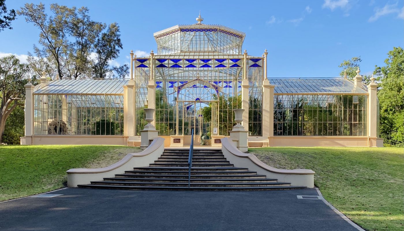 Symmetrical glass conservatory with a raised central pavilion, broad steps, and lawns on either side.